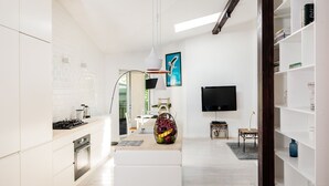 A modern kitchen with white cabinetry, a built-in oven, and a dining area with a table and chairs. - All In Apartments (Kraków)