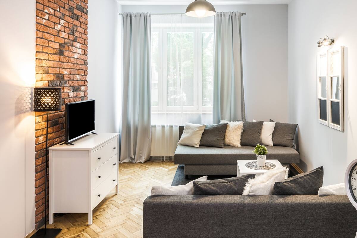 A modern living room with a sofa, a TV, a small table with a plant, and a clock on the wall.