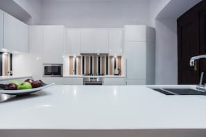 A modern kitchen with white cabinetry, a central island with a sink, and a bowl of apples.
