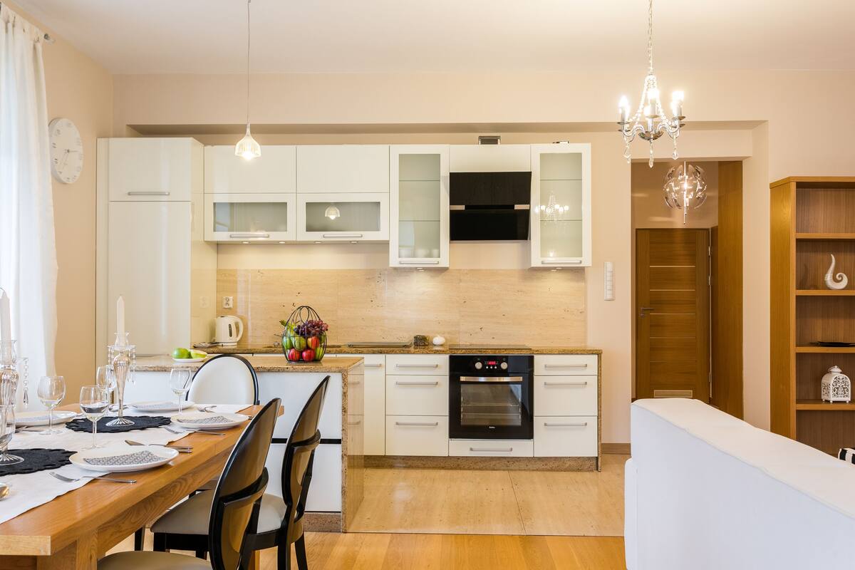 A modern kitchen with white cabinets, a built-in oven, and a dining area with a wooden table and chairs.