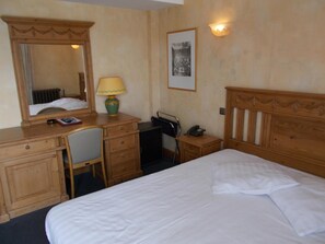 A hotel room with a bed, a desk with a lamp, a chair, a telephone, and a framed picture on the wall. - Hotel Manitoba (Blankenberge)