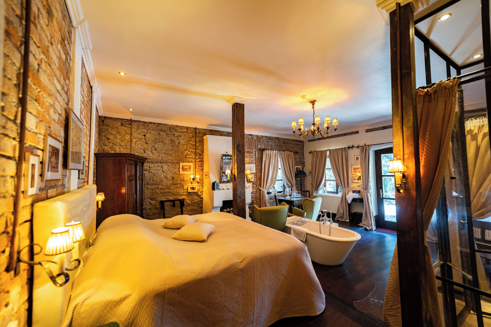 Una habitación de hotel con una cama grande, una bañera, paredes de piedra y un candelabro.