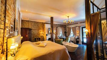 Una habitación de hotel con una cama grande, una bañera, paredes de piedra y un candelabro.
