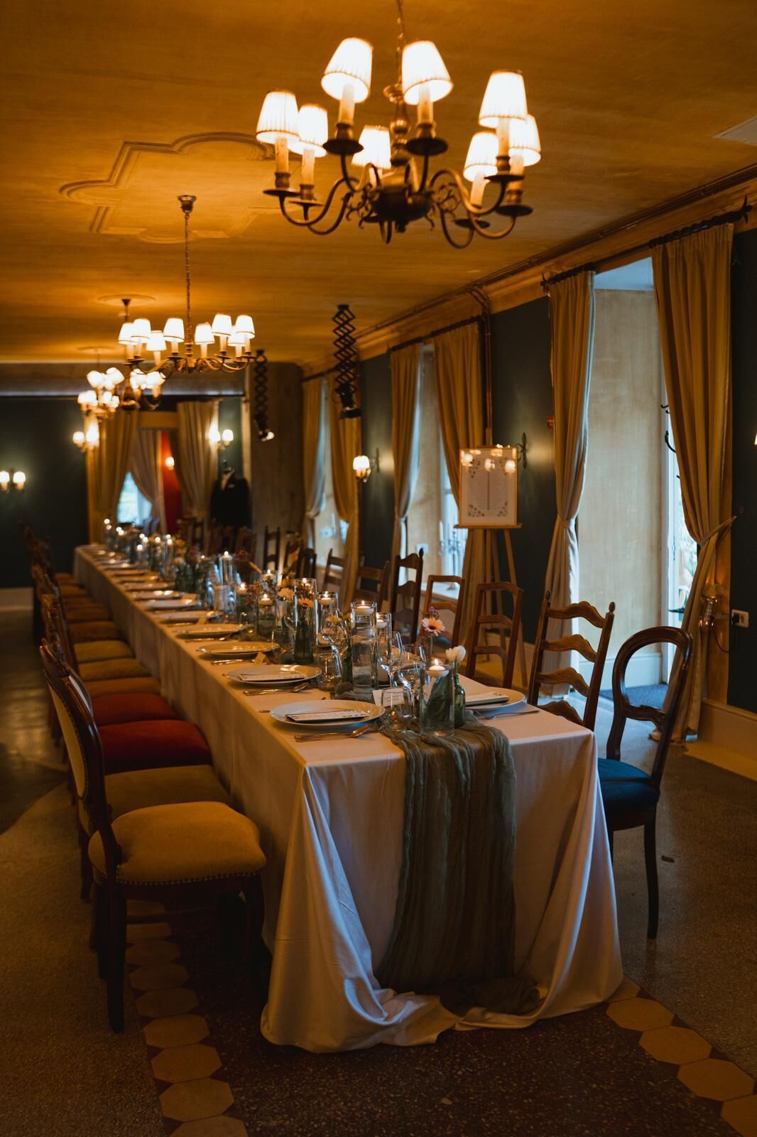 A long dining table set with chairs, chandeliers, and a view of the outdoors.