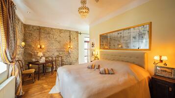 A bedroom with a large bed, a stone wall, a chandelier, and a painting on the wall.