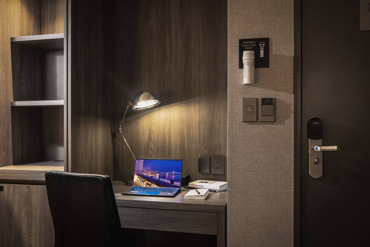 Une chambre d’hôtel avec un bureau en bois, un ordinateur portable, une lampe, un téléphone et une porte dotée d’une serrure à carte magnétique.