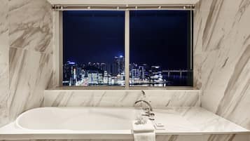 Un baño moderno con una bañera amplia, una ventana con vistas a la ciudad y paredes de mármol.