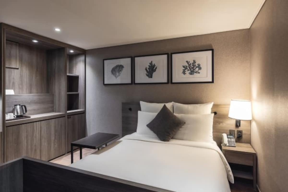 A hotel room with a bed, bedside table, lamp, and a small kitchenette area.
