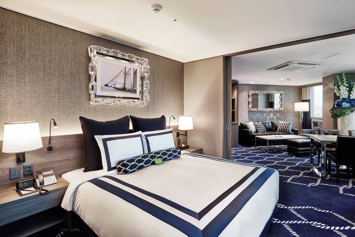 Une chambre d’hôtel avec un grand lit, des lampes de chevet, un bureau avec une chaise, un miroir et une vue sur la ville par la fenêtre.