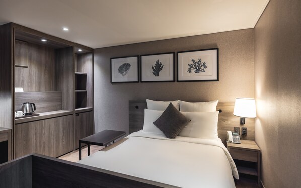 A modern hotel room with a bed, bedside table, lamp, and a built-in desk with a kettle. - Kent Hotel Gwangalli by Kensington (Busan)