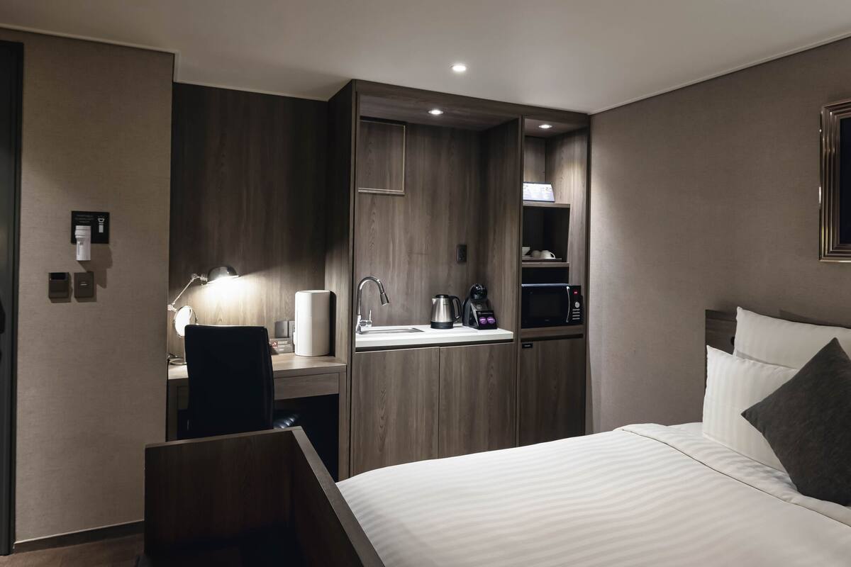 Une chambre d’hôtel comprenant un lit, un bureau avec une lampe, une machine à café et un lavabo intégré.
