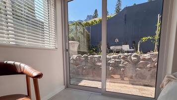 Quarto com porta de vidro deslizante que dá para um pátio exterior com parede de pedra, mesa e cadeiras.