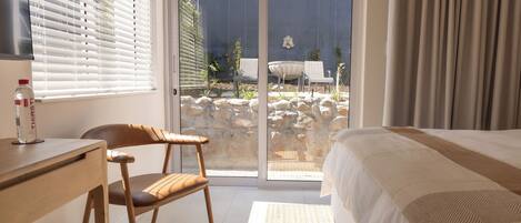 A bedroom with a bed, a desk, a chair, and a view of an outdoor area with a pool and plants.