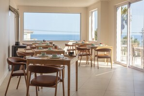 A dining area with multiple tables and chairs, large windows with a view of the sea, and a modern interior design. - Finchley Guest House (Cape Town)