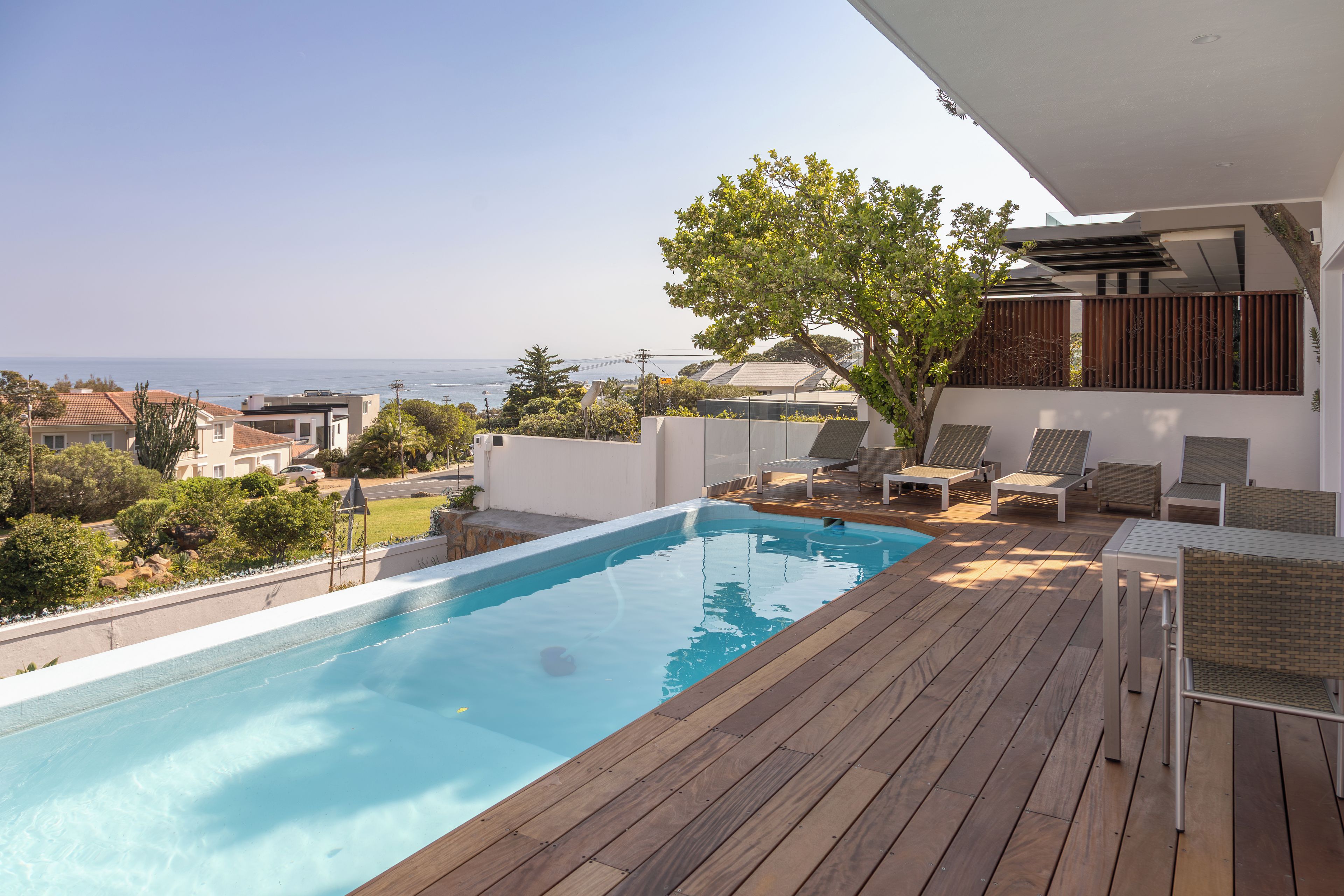 A swimming pool with a wooden deck, lounge chairs, and a view of the sea.