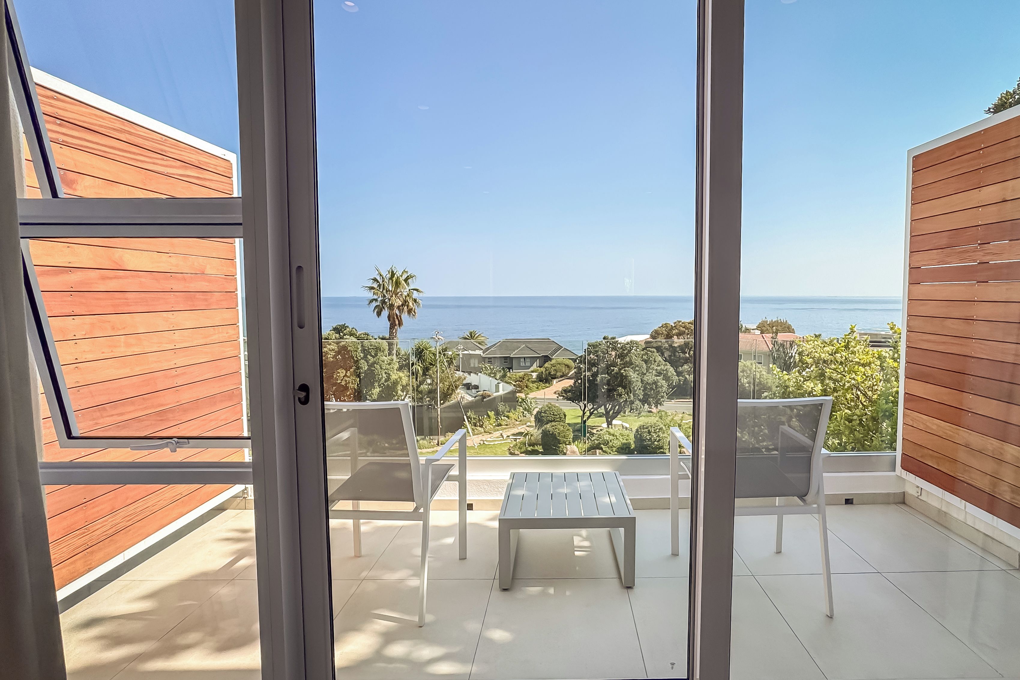 A balcony with a view of the sea, a palm tree, and a chair.