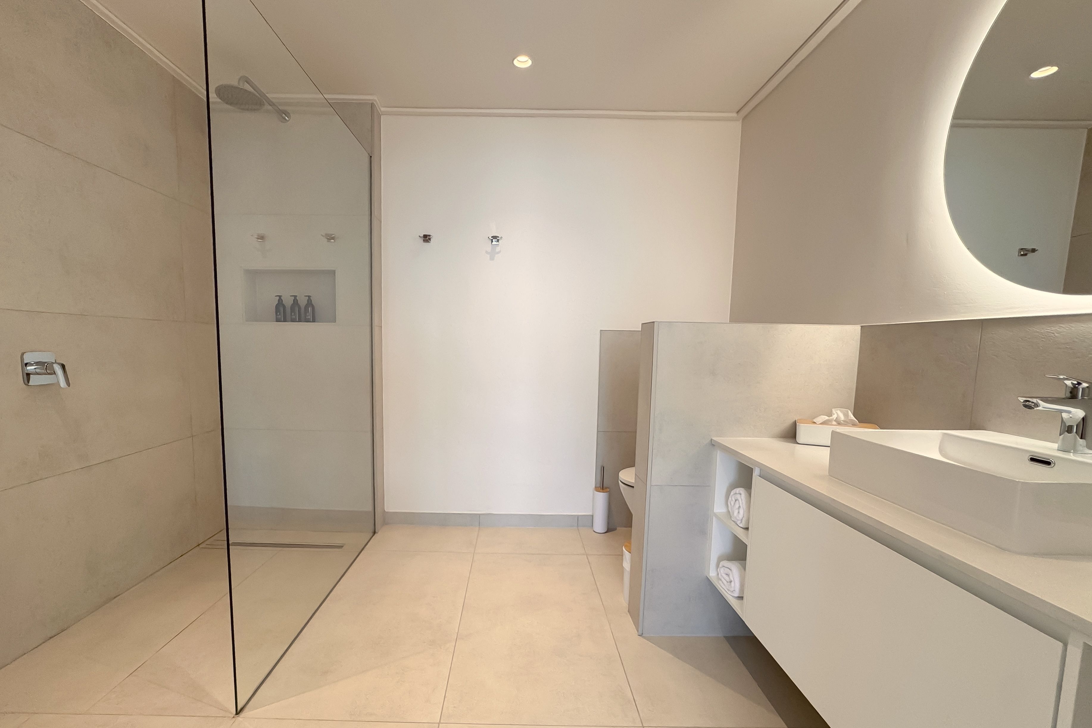 Um banheiro moderno com chuveiro em gabinete de vidro, toucador branco com espelho grande e vaso sanitário com porta-toalhas.