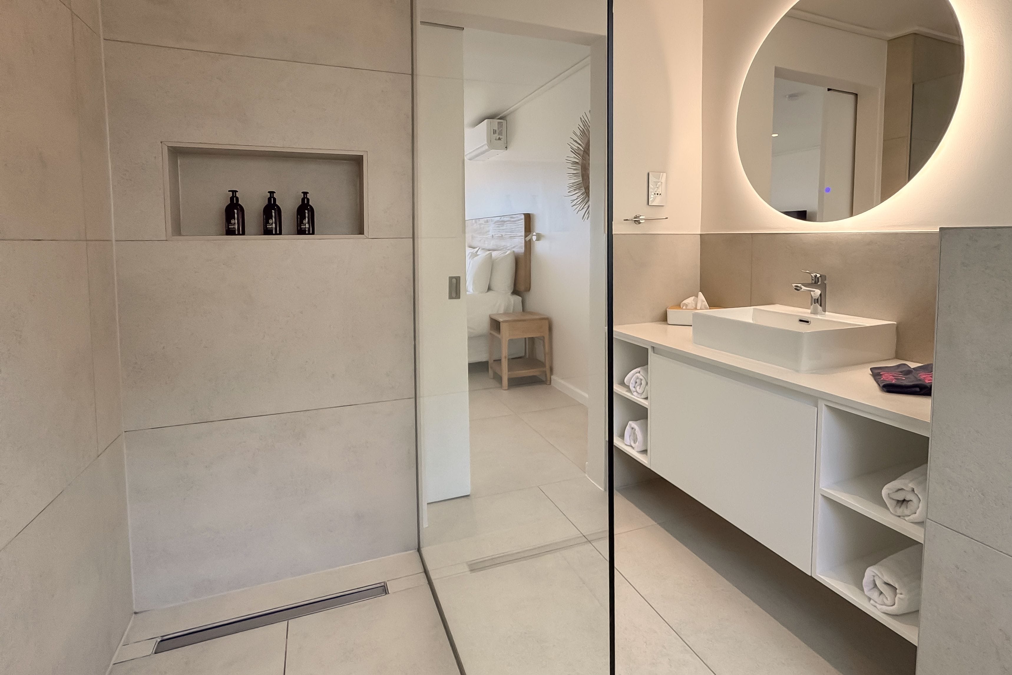 A modern bathroom with a built-in shelf holding toiletries, a large mirror, and a vanity with a sink and towel storage.