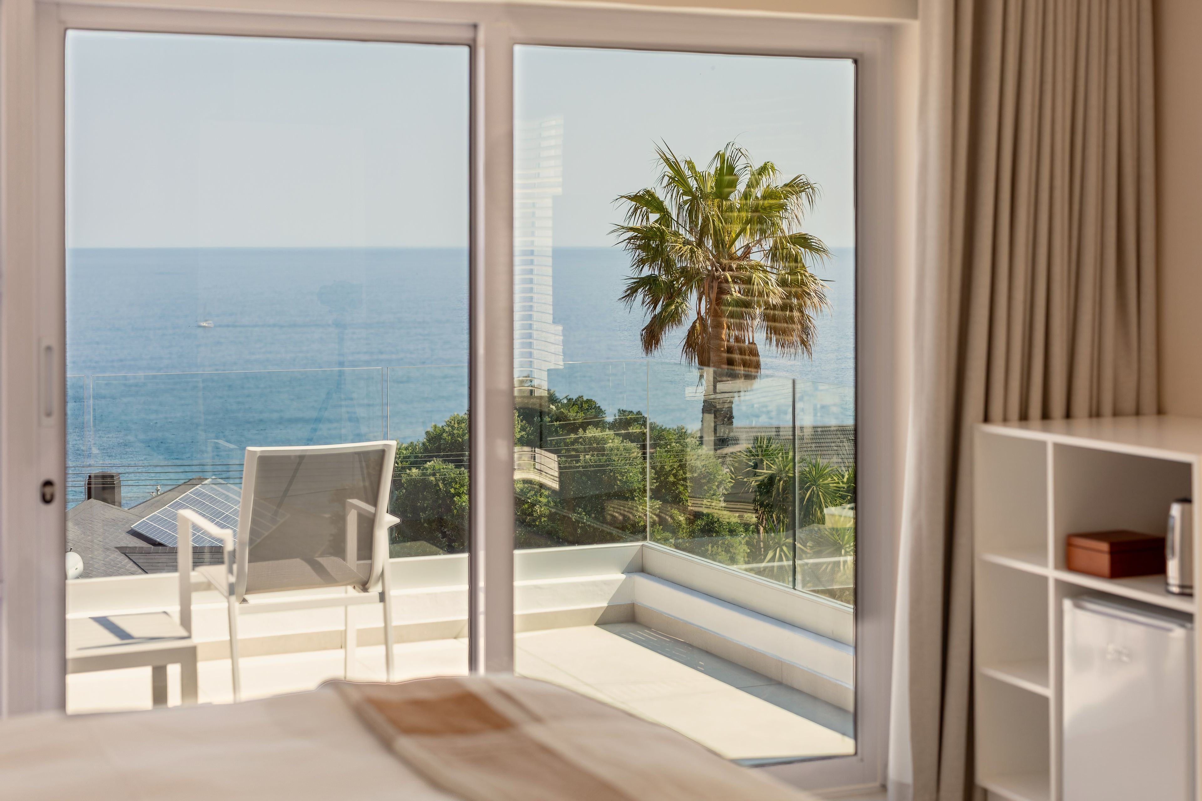 Una habitació amb balcó i vista al mar, una cadira i un llit.
