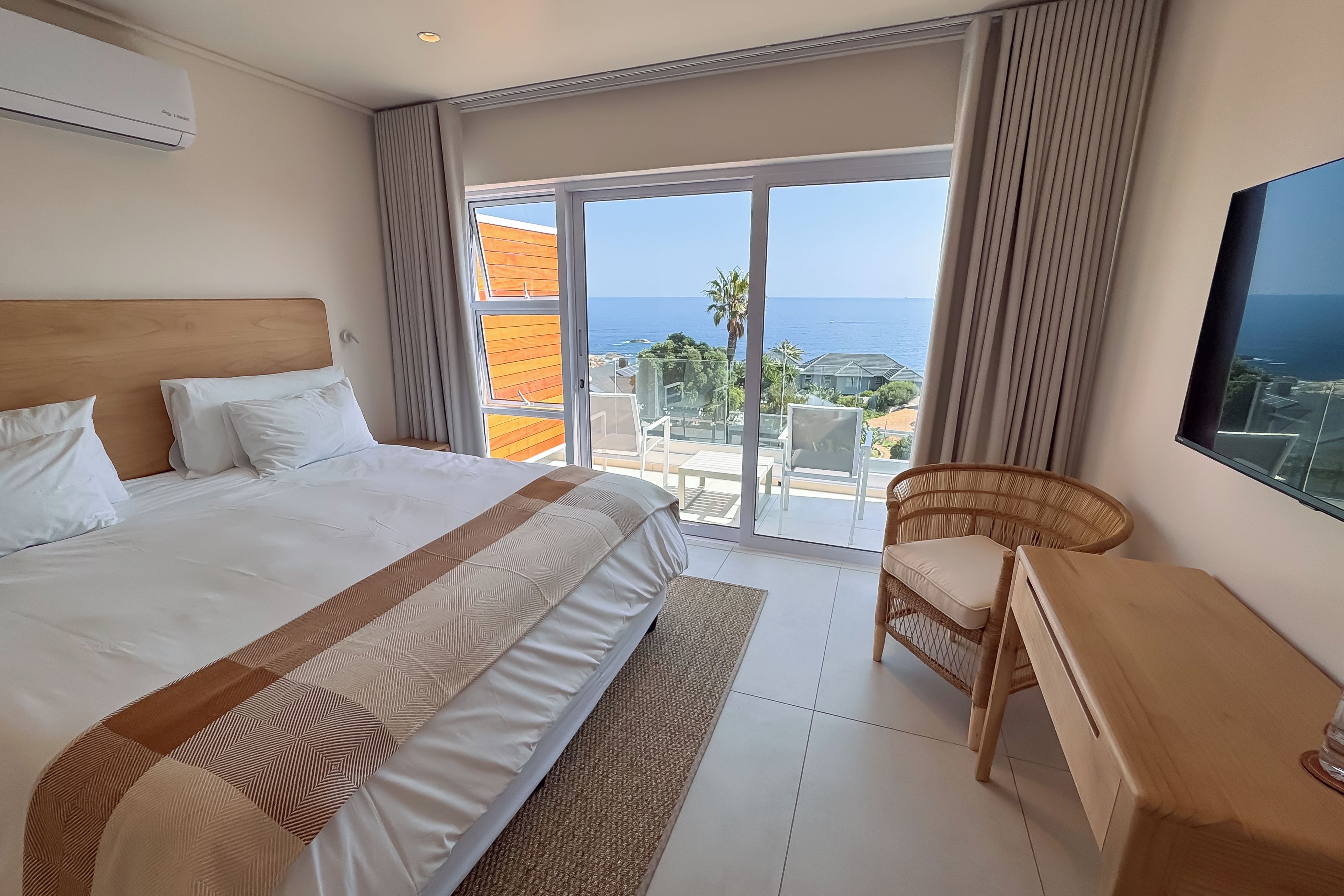 A hotel room with a large bed, a desk, a chair, and a view of the sea through a sliding glass door.