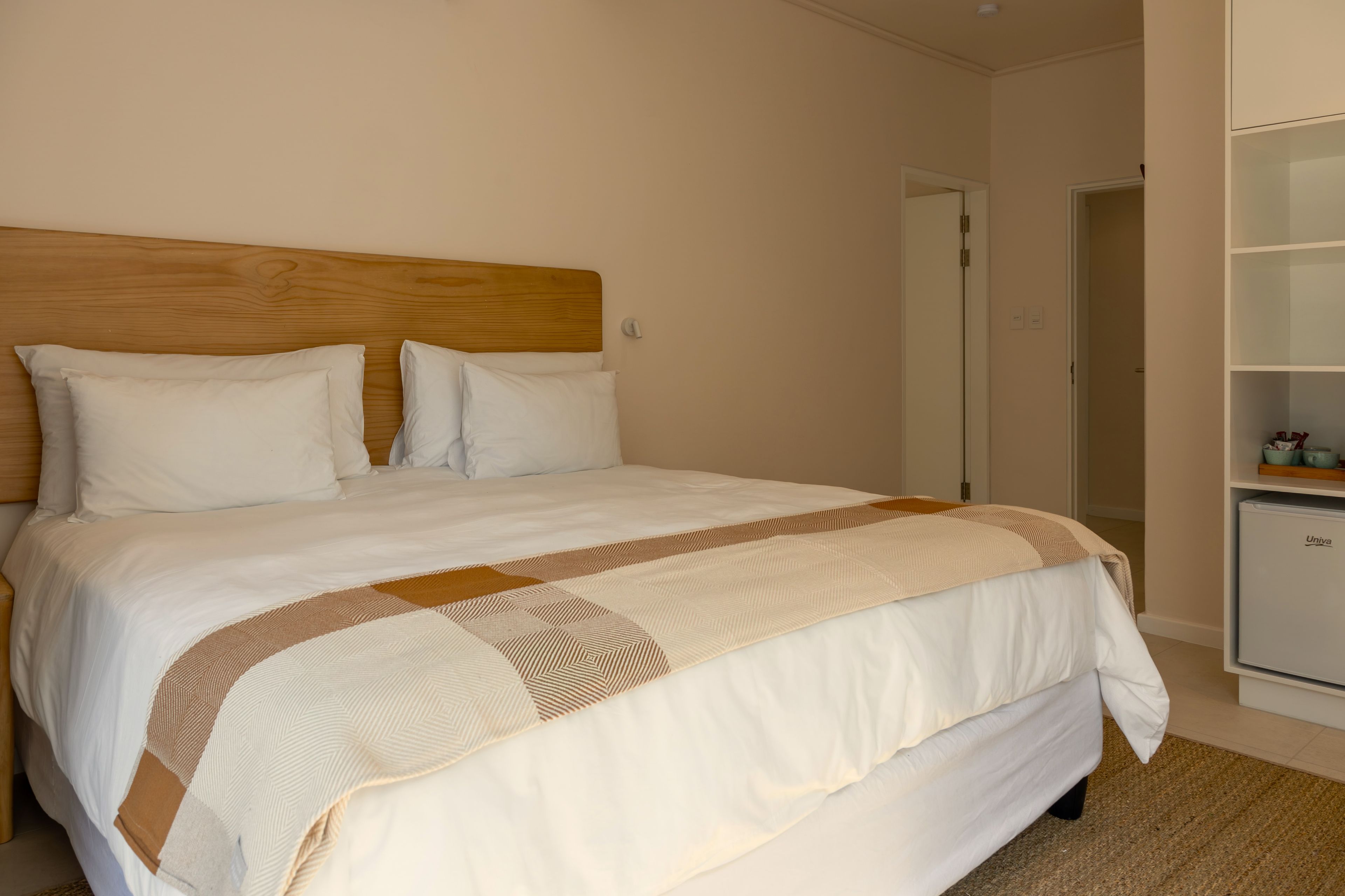 A neatly made bed with a wooden headboard, white bedding, and a patterned throw.