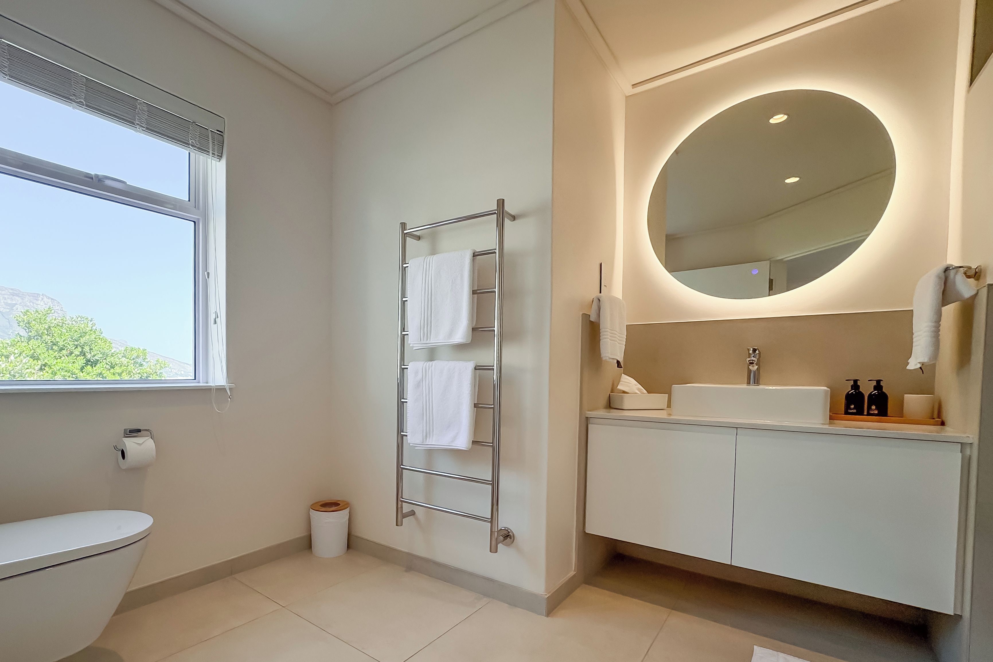 Uma casa de banho moderna com sanita, um porta-toalhas, uma pia com espelho e uma janela.