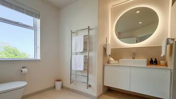 Uma casa de banho moderna com sanita, um porta-toalhas, uma pia com espelho e uma janela.