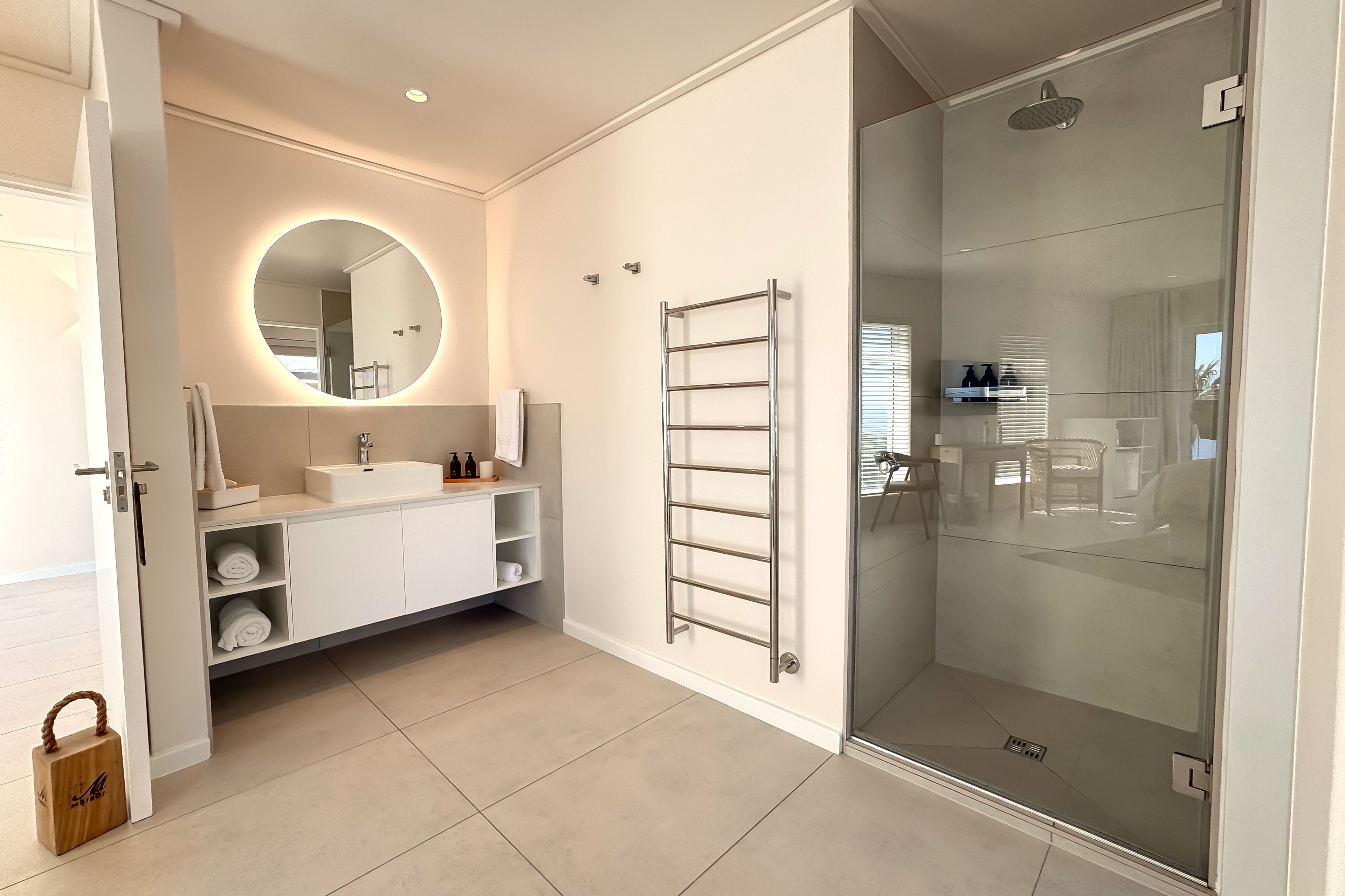 A modern bathroom with a glass shower enclosure, a round mirror, and a white vanity with a towel rack.