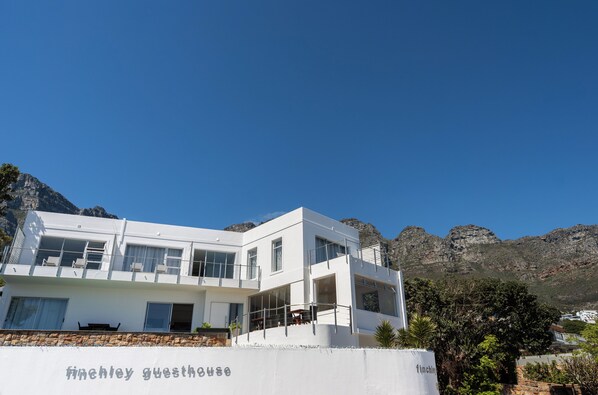 A modern white building with balconies, labeled "Finchley Guesthouse," set against a mountainous backdrop. - Finchley Guest House (Cape Town)