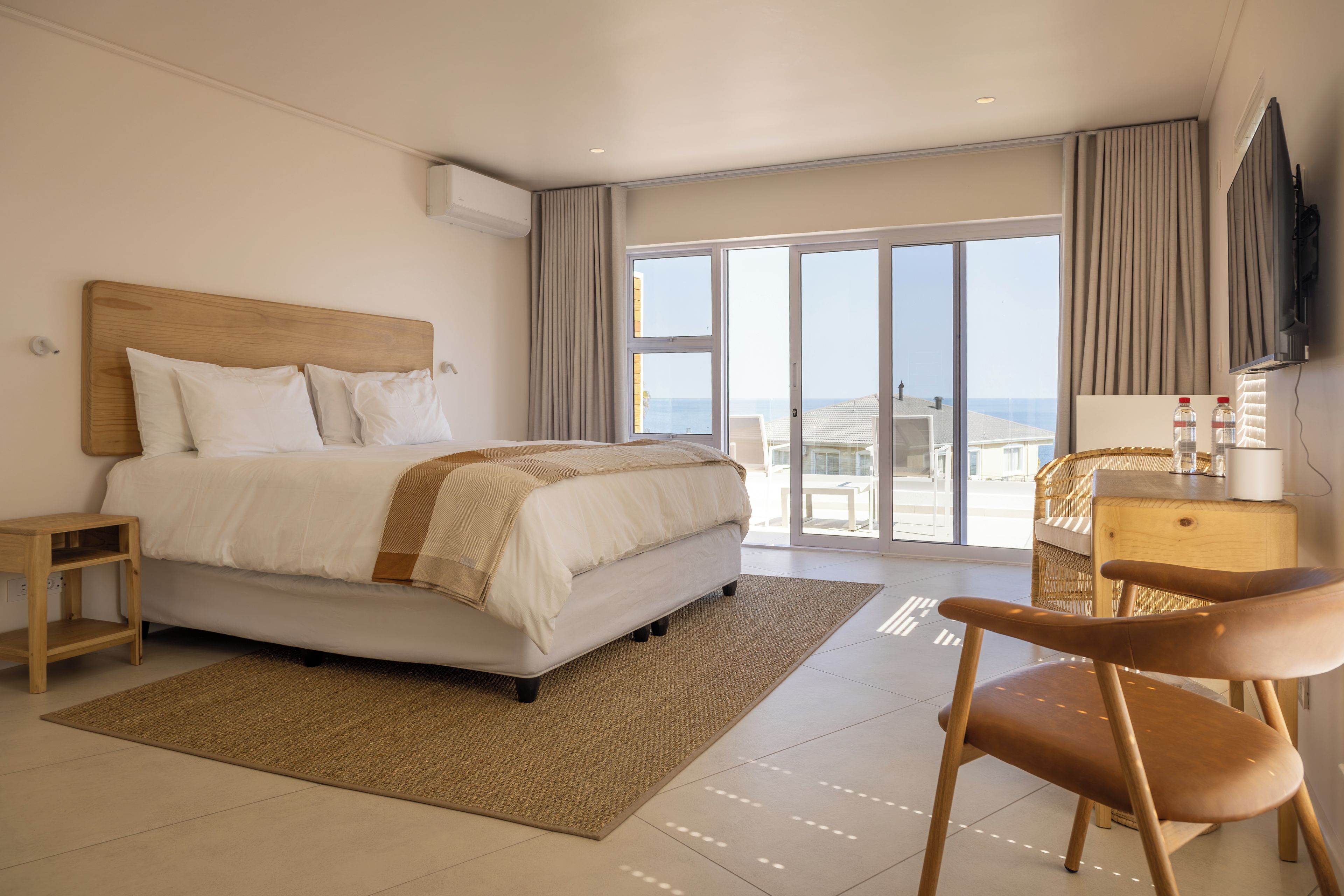 Habitación de hotel con cama, escritorio, silla, televisión y vista al mar.