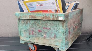 A wooden cart with wheels filled with various items, including books and papers, placed on a black surface against a wall.