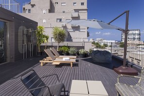A rooftop terrace with wooden lounge chairs, a table, and potted plants. - Florentin House - By HOMY (Tel Aviv)