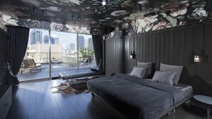 Une chambre moderne avec un grand lit, une vue sur la ville et un balcon aménagé avec des sièges.