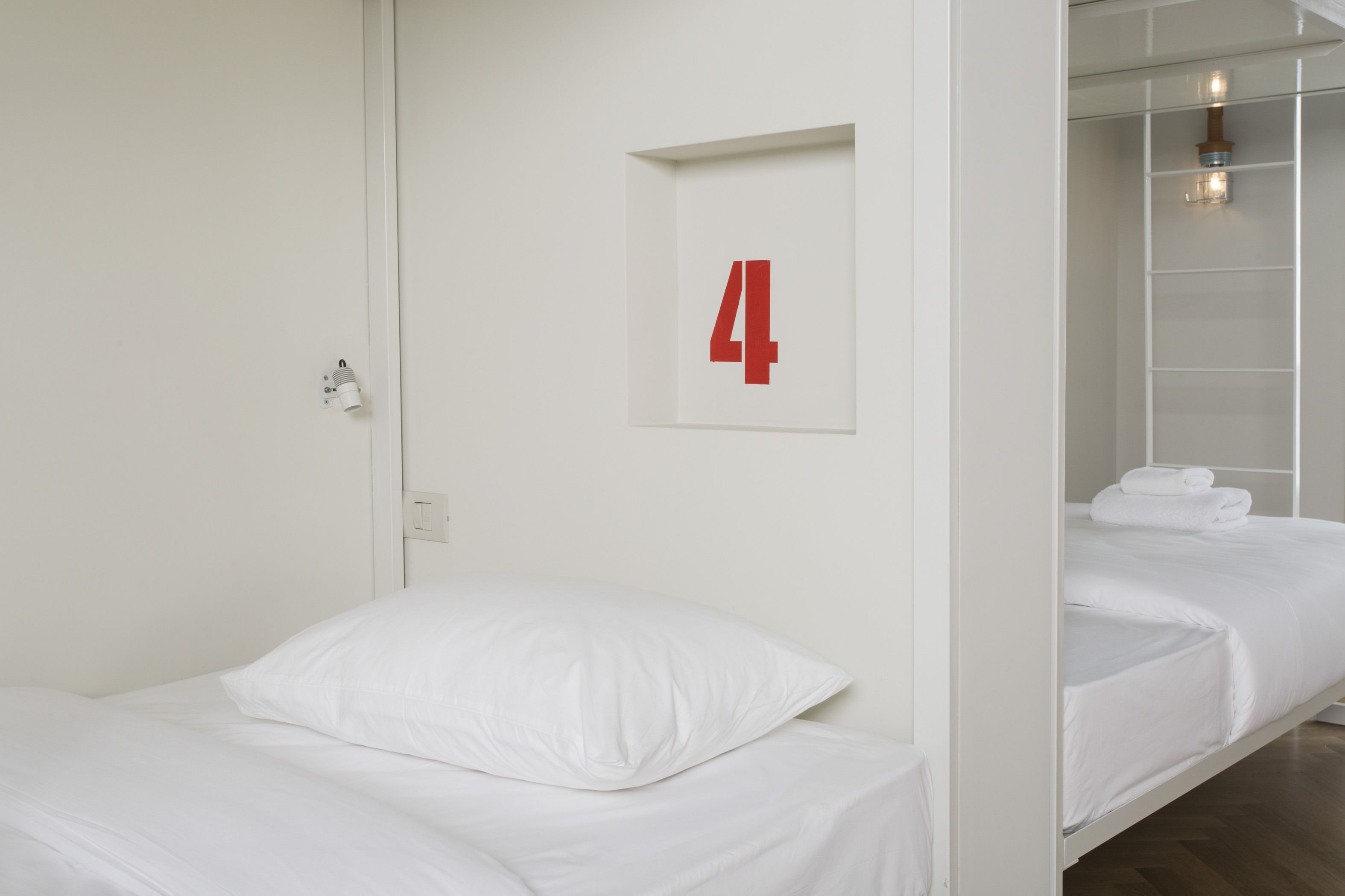 Une chambre d’hôtel avec un lit, un numéro « 4 » fixé au mur et une salle de bain équipée d’un porte-serviettes.