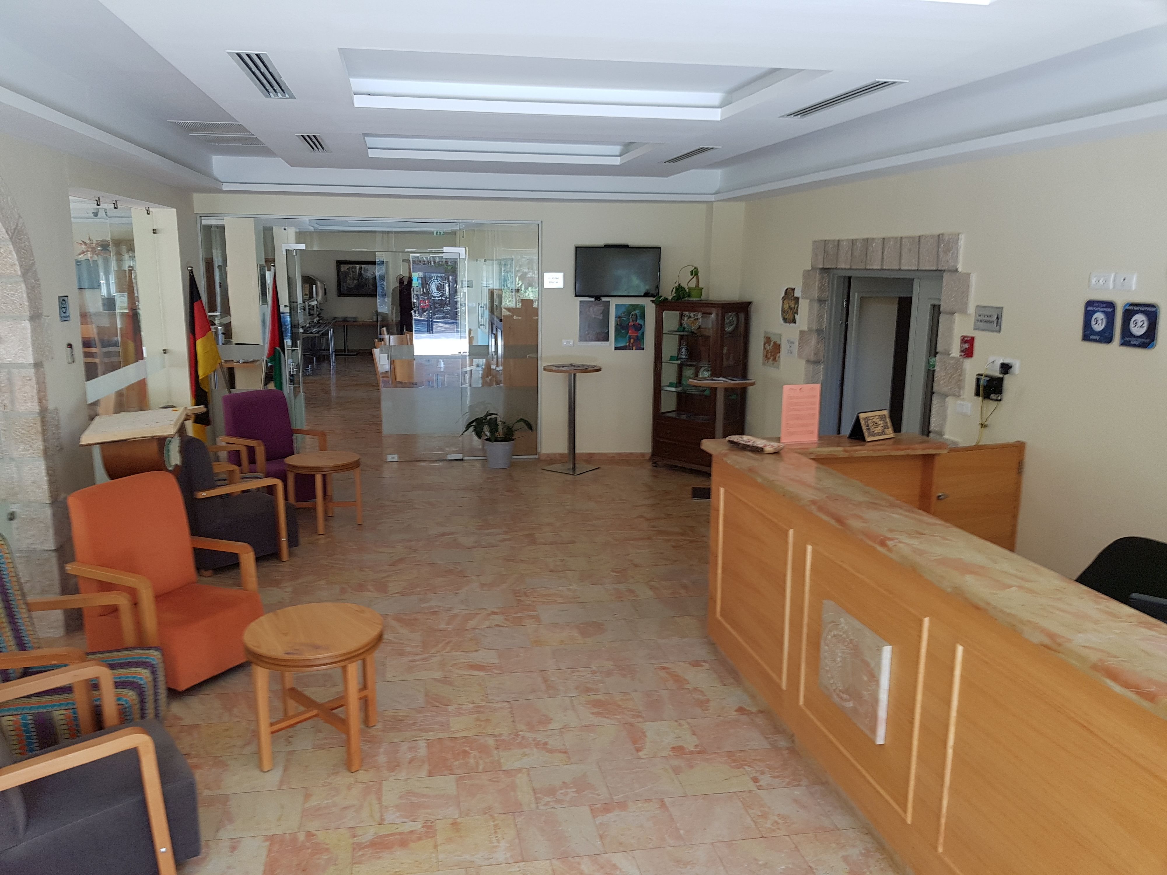 Un hall de hotel con mostrador de recepción, área de descanso con sillas y mesas, un televisor y una chimenea.