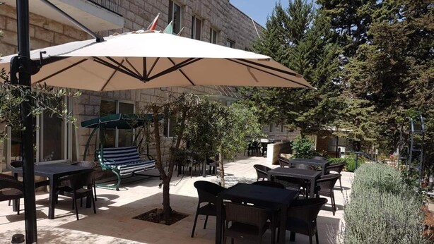 Een terras buiten met tafels en stoelen, een grote parasol en een stenen gebouw op de achtergrond.