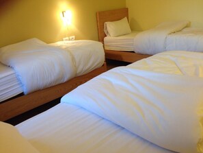 Ein Hotelzimmer mit drei Einzelbetten, jedes mit weißer Bettwäsche und einem Holz-Kopfteil.