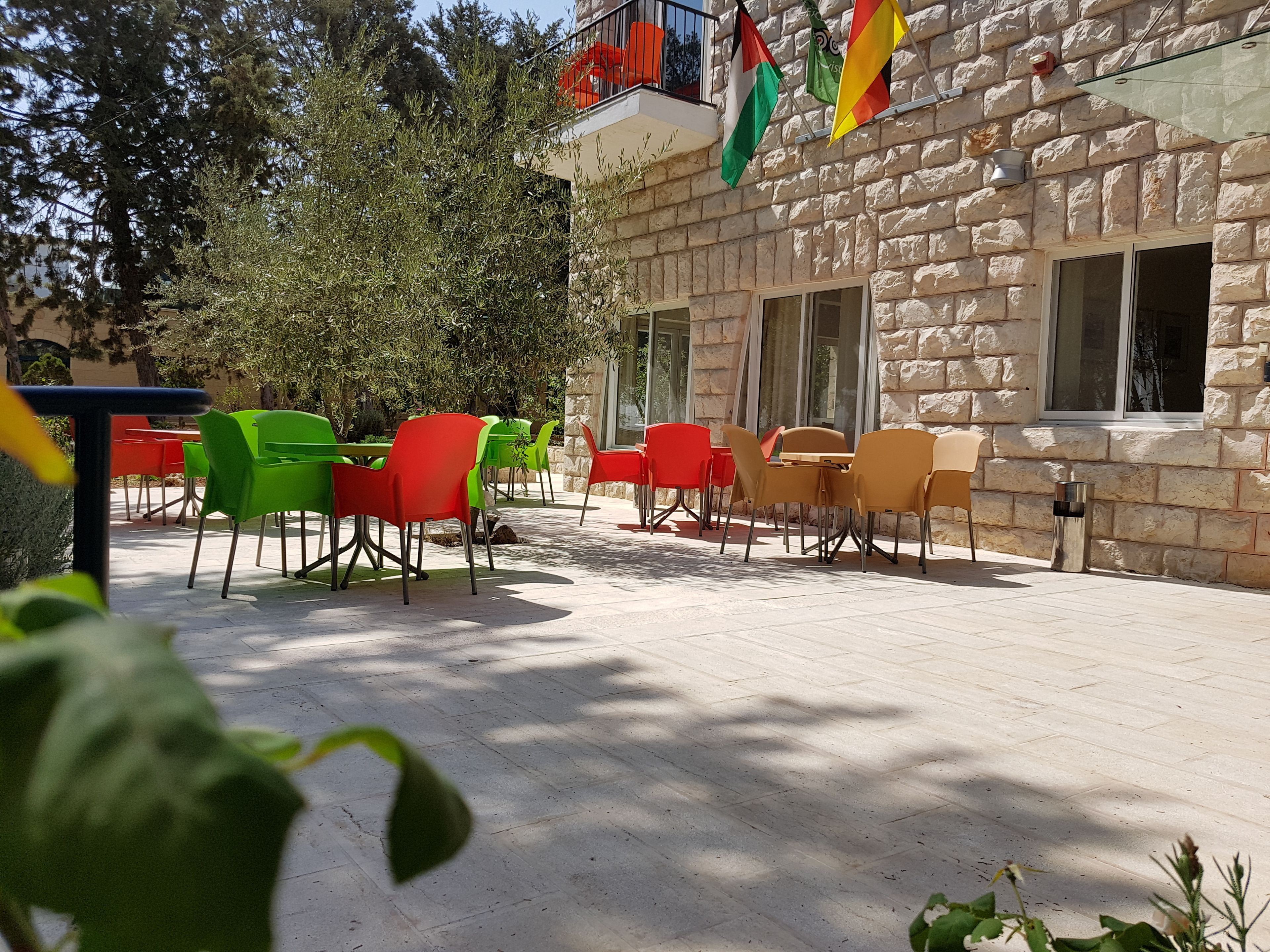 An outdoor seating area with tables and chairs, stone walls, and flags.