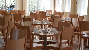 Een eetgedeelte met houten tafels en stoelen, ruim opgezet met grote ramen voor veel daglicht.