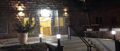 A stone building with a glass entrance, outdoor lighting, and a staircase leading to the entrance.