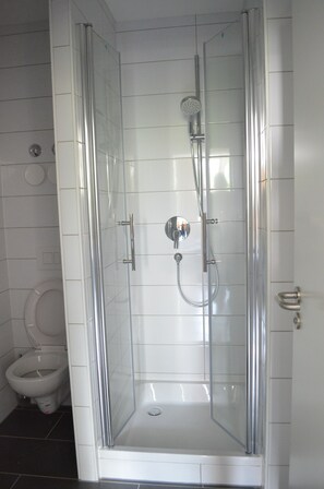Cabina de ducha con paredes de vidrio, cabezal de ducha de mano y llave de pared.