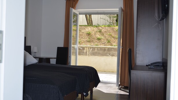 A bedroom with a bed, a desk, a chair, a TV, and a sliding glass door leading to a balcony. - Zwei Raben Pension (Mainz)