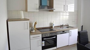 A modern kitchen with white cabinets, a stainless steel range hood, a built-in oven, and a double sink. - Zwei Raben Pension (Mainz)