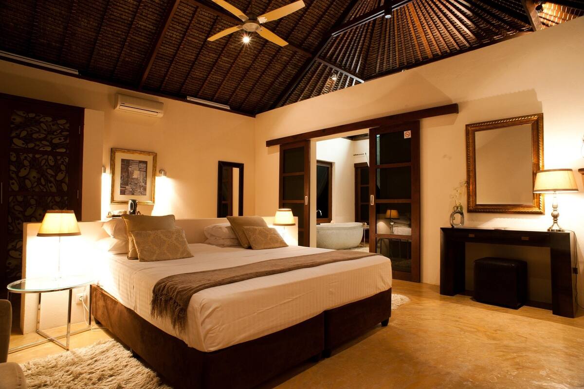A spacious bedroom with a large bed, bedside lamps, a ceiling fan, and a wooden floor.
