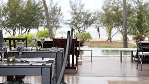 An outdoor dining area with tables set for a meal, overlooking a body of water and trees. - Chuiba Bay Lodge (Pemba)