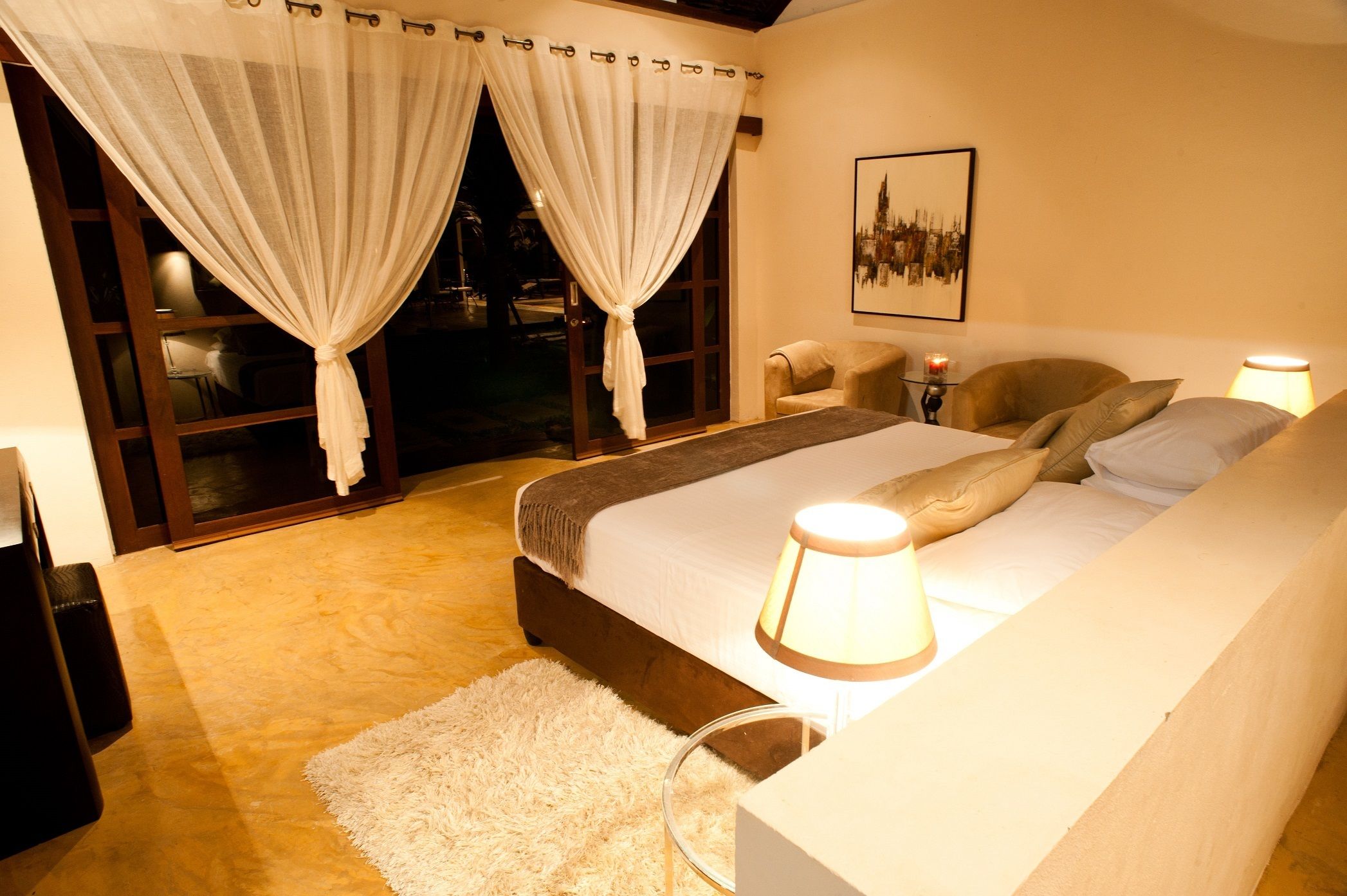 A bedroom with a bed, two chairs, a lamp, a rug, and a window with curtains.