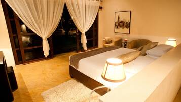 A bedroom with a bed, two chairs, a lamp, a rug, and a window with curtains.