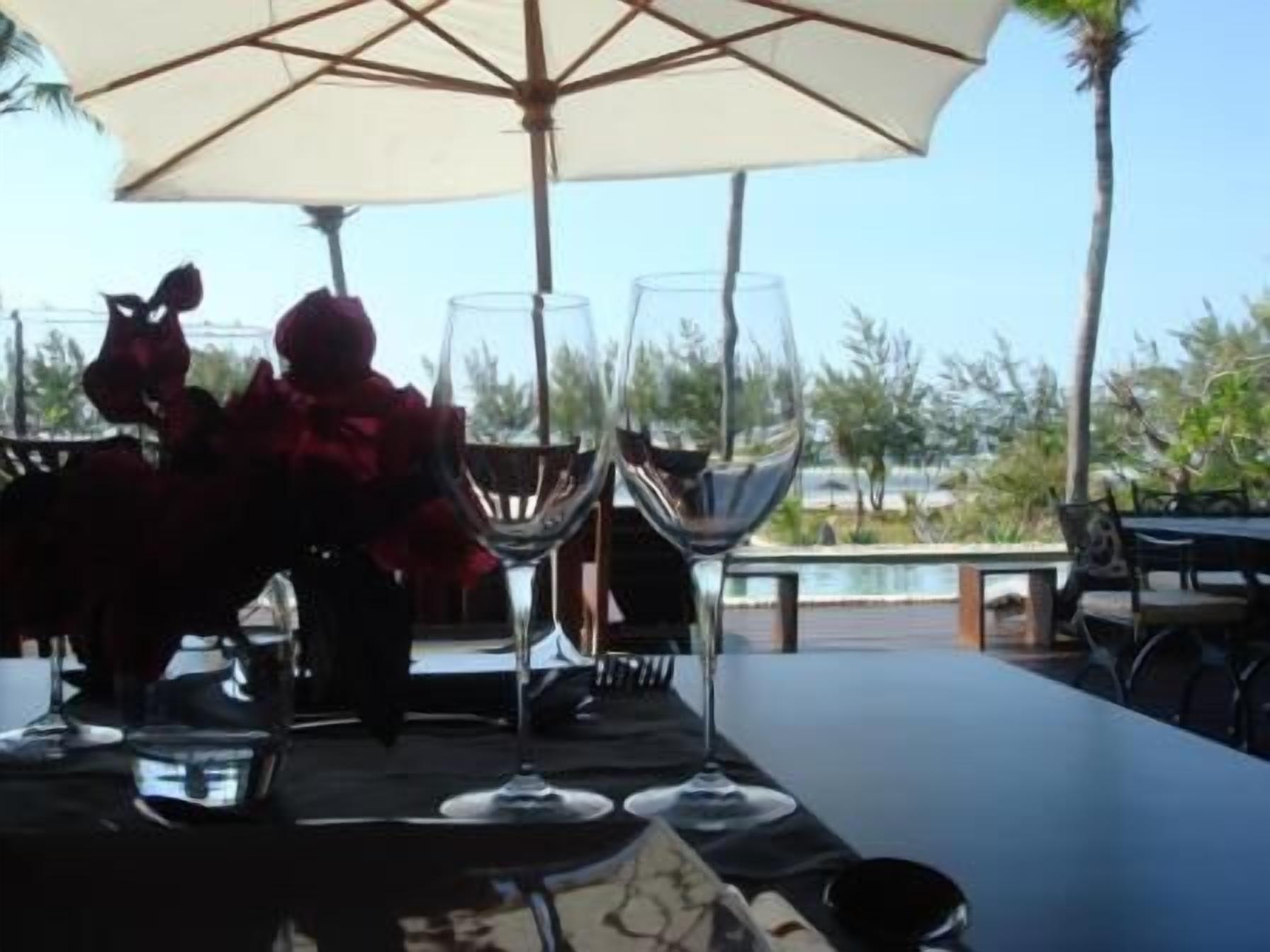Un área de comedor al aire libre con una mesa dispuesta para dos personas, dos copas de vino y un paraguas grande.