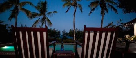Two striped lounge chairs facing a pool with palm trees in the background.