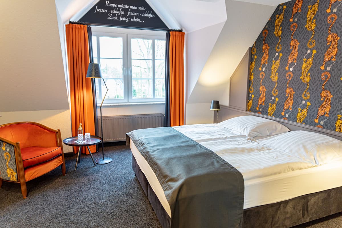 A hotel room with a bed, a chair, a small table, and a window with curtains.